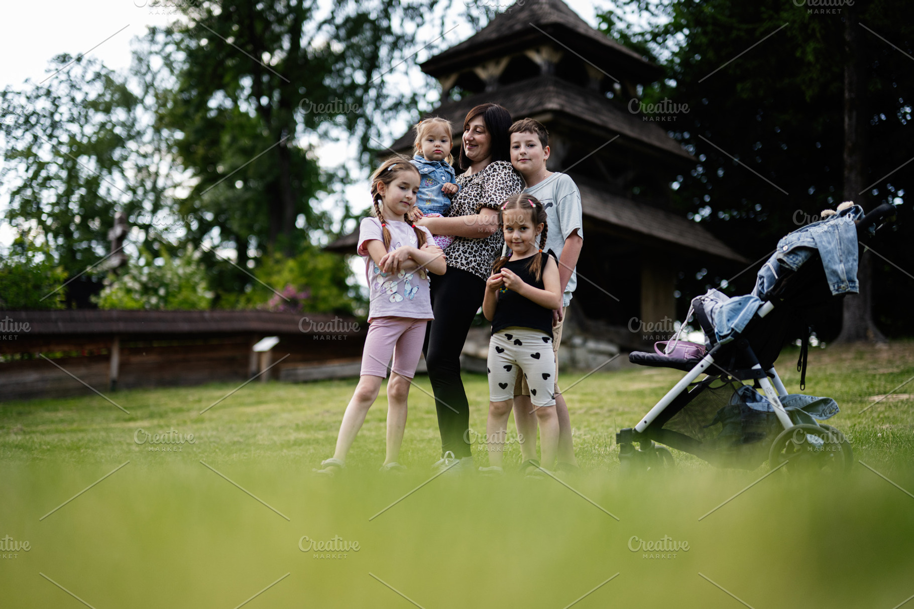 Mother standing with children near stroller in lush green outdoors setting, a Person Photo by AS photostudio