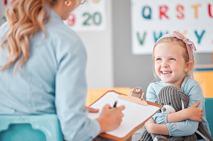 Smiling little girl with social worker in a clinic. Child psychologist writing on a clipboard during consult with adorable kid. Caucasian woman signing adoption paperwork while girl holds a teddy bear, a Photo by Peopleimages.com