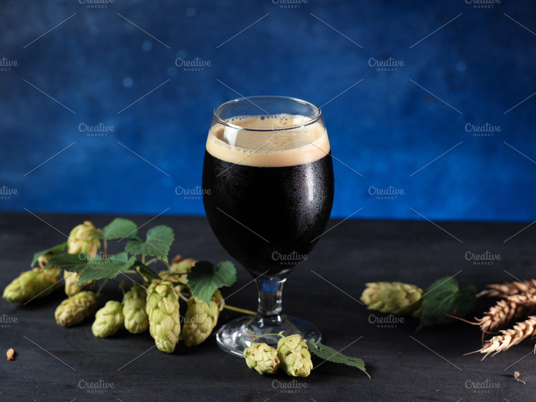 A glass of beer stout or porter on a dark blue background, green cones of hops, a Food & Drink Photo by PavelKant