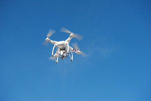 Quadrocopter unmanned camera hovers in bright blue sky containing aircraft