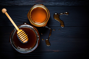 Honey in glass jar on wooden background, a Food & Drink Photo by AlyaAnd