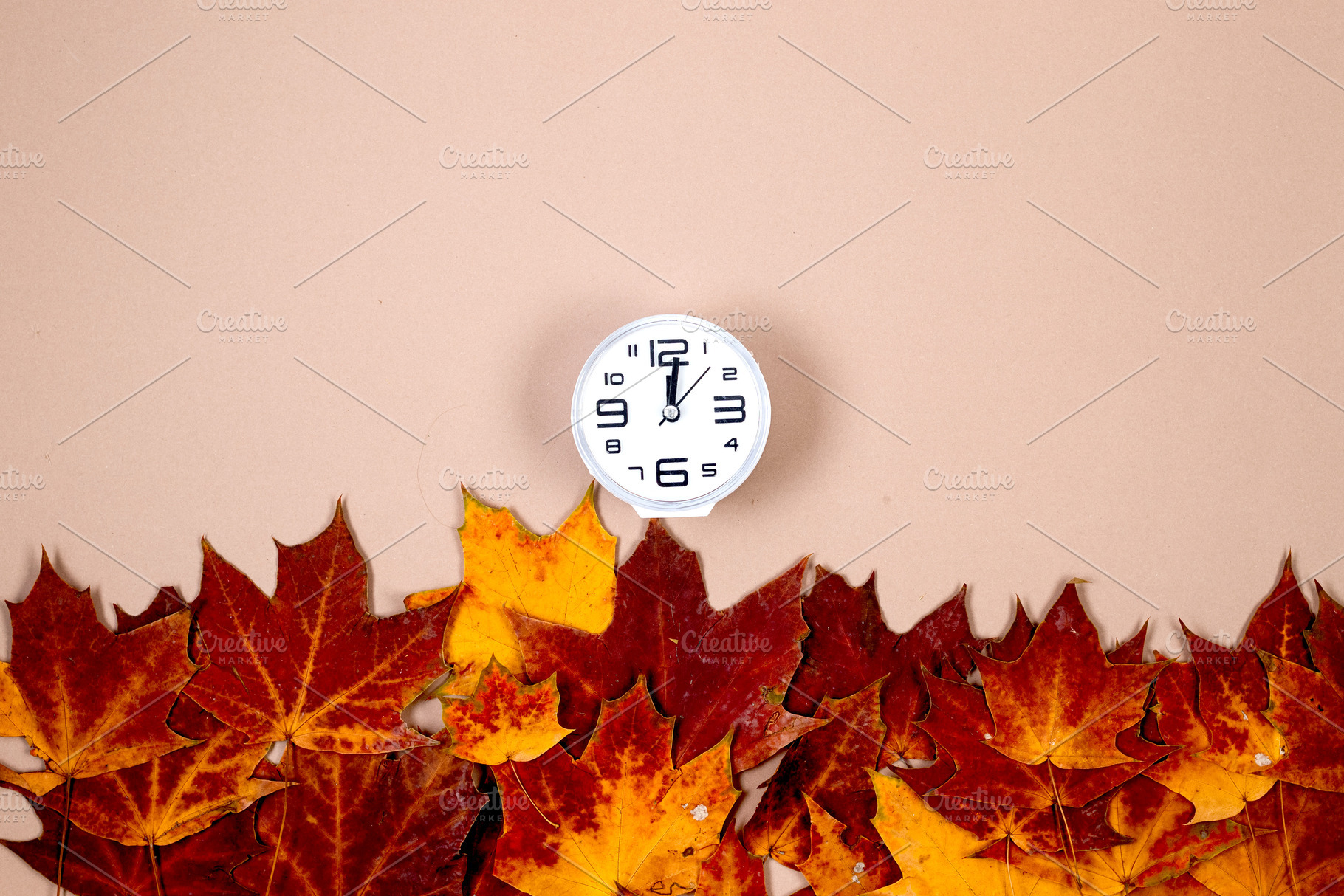 Clock and autumn leaves on beige background, saving winter time, a Business Photo by vimart