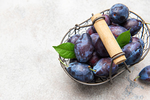 Fresh purple plums in wire basket on concrete, a Food & Drink Photo by Olena Rudo