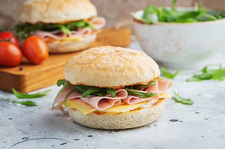 Two homemade sandwiches with ham, cheese and arugula on a concrete table., a Food & Drink Photo by Budarinphoto