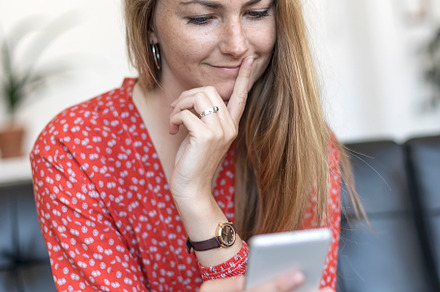Smiling woman at home sitting on couch looking at cell phone, a Person Photo by 2Design