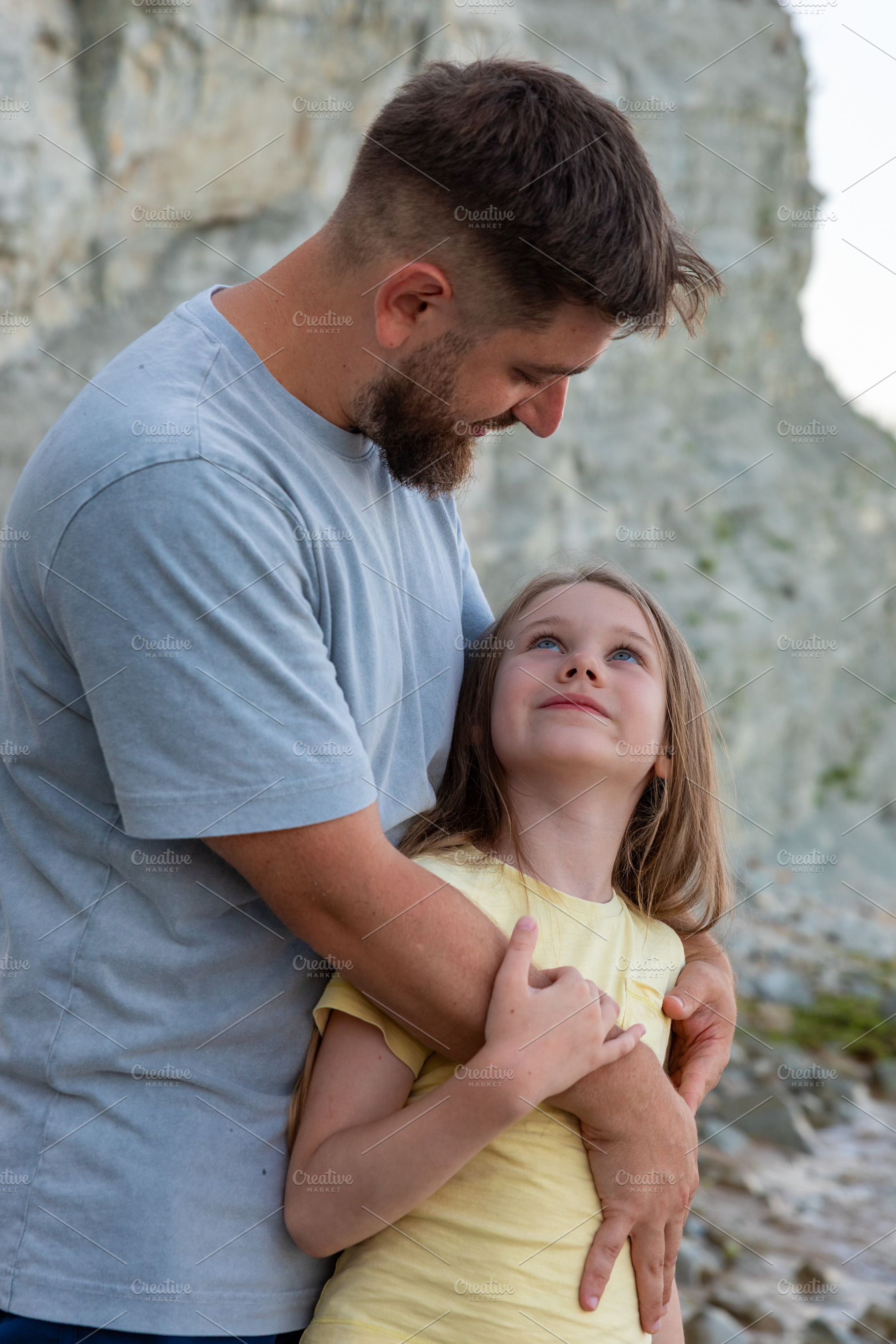 Happy father hugging his daughter on a rocky outdoor landscape with a cliff bac, a Person Photo by Ales Munt