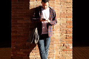 Young caucasian man using smartphone against brick wall, a Person Photo by RF Images