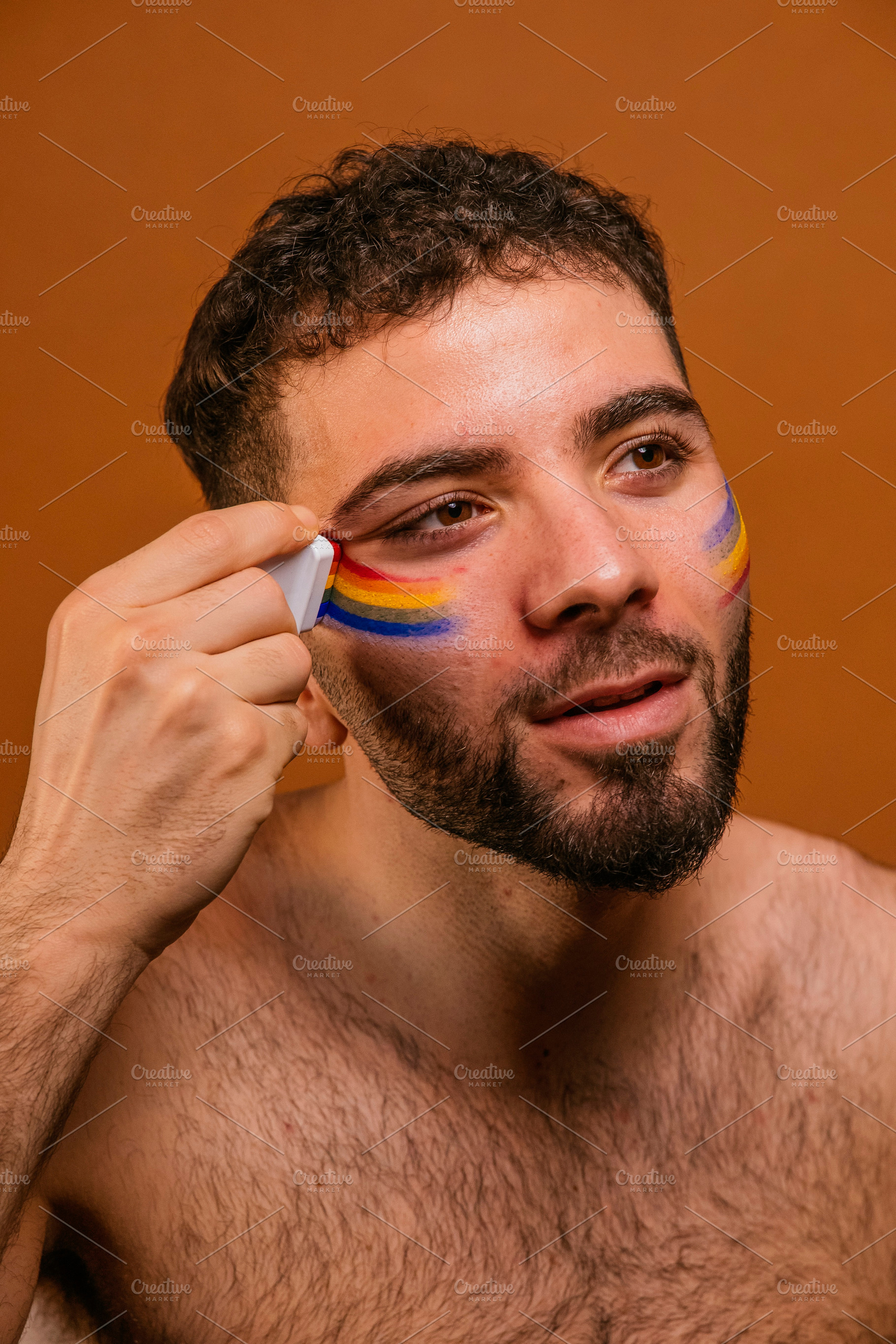 Man applying rainbow face paint for pride celebration, a Photo by karrastock