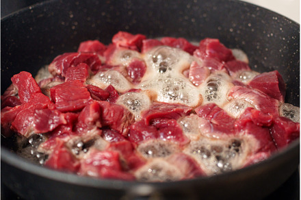 Chunks of raw beef are sizzling in a