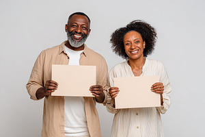 Happy couple holding blank sheets of paper in a neutral studio background, a Photo by AlyaAnd