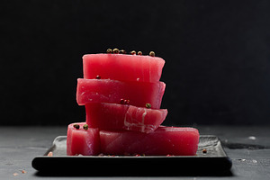 Stack of raw tuna pieces on black plate, black table, a Food & Drink Photo by ndanko