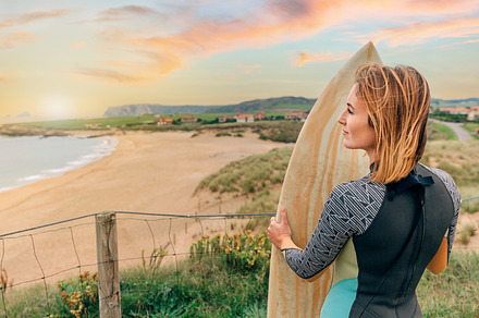 Surfer woman with wetsuit and surfboard looking at the beach, a Sports & Recreation Photo by davidpereiras