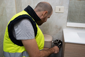 Plumber repairing toilet water valve in home bathroom, a Person Photo by etorres69
