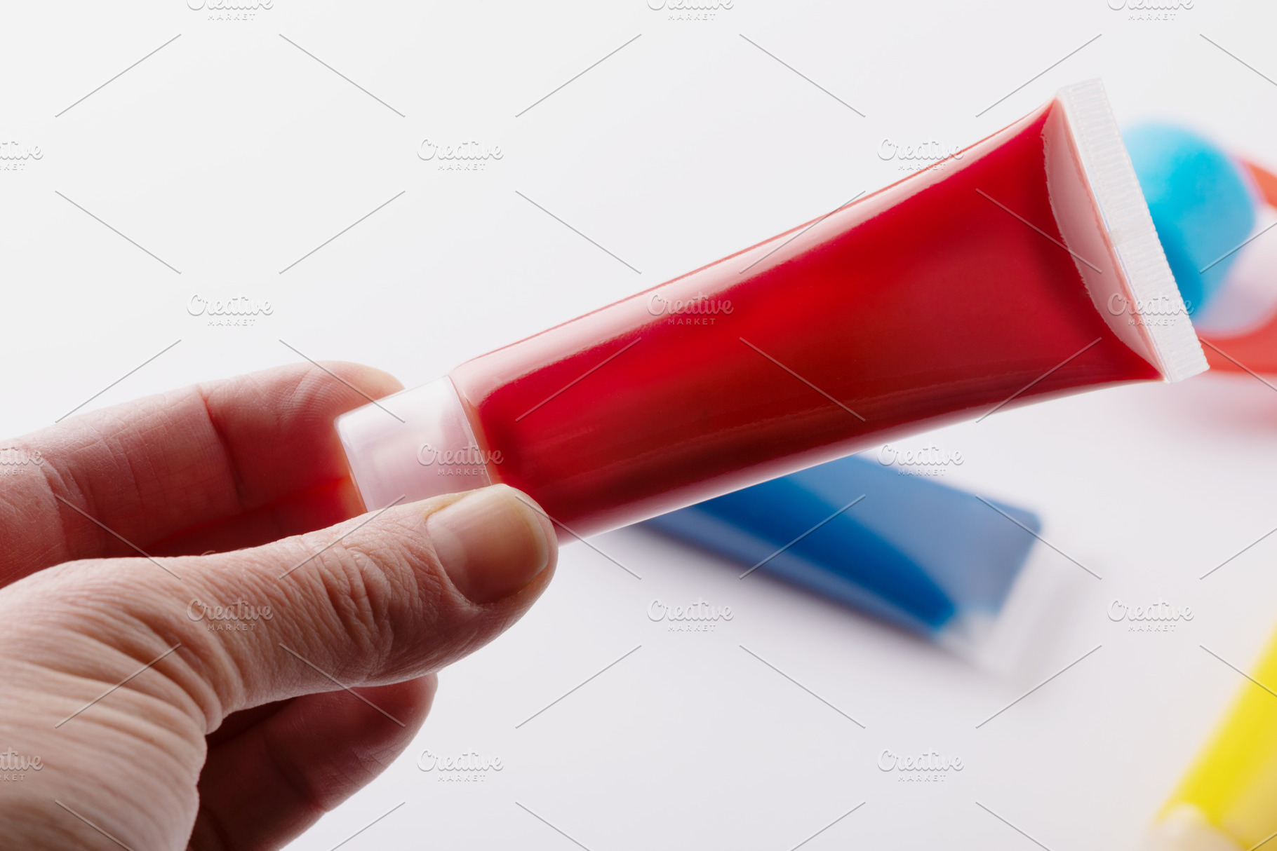 Close-up of a hand holding a red paint tube with blurred blue an, a Holiday Photo by Ales Munt