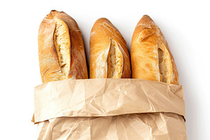 Freshly baked baguette in paper bag isolated on white background, a Food & Drink Photo by AlyaAnd