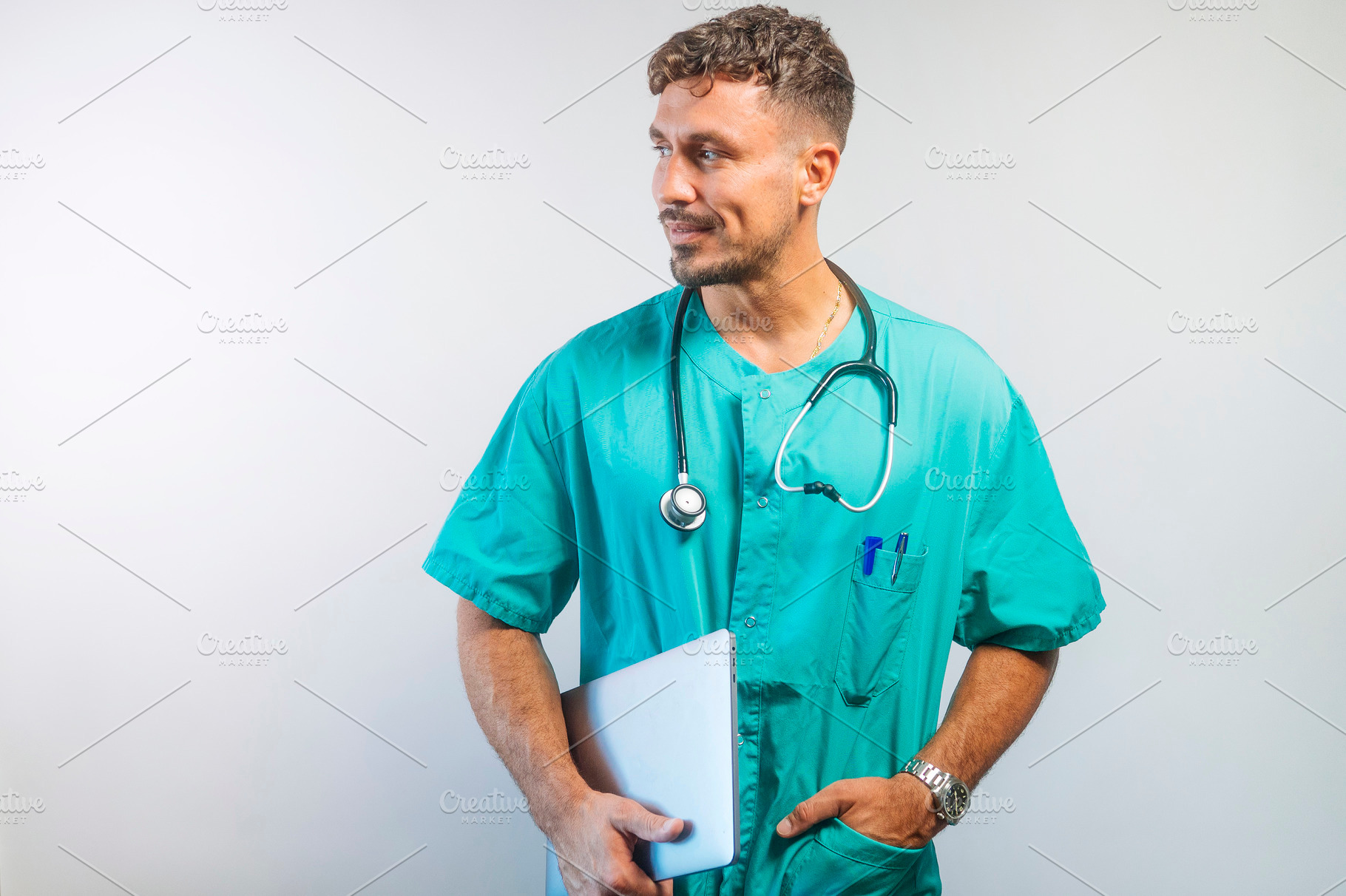 Male doctor holding a tablet and looking to the side, dressed in green scrubs w, a Person Photo by karrastock