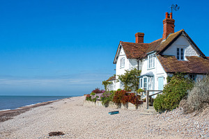White cottage standing on a pebble beach with a gentle ocean and, a Photo by Studio ANNA