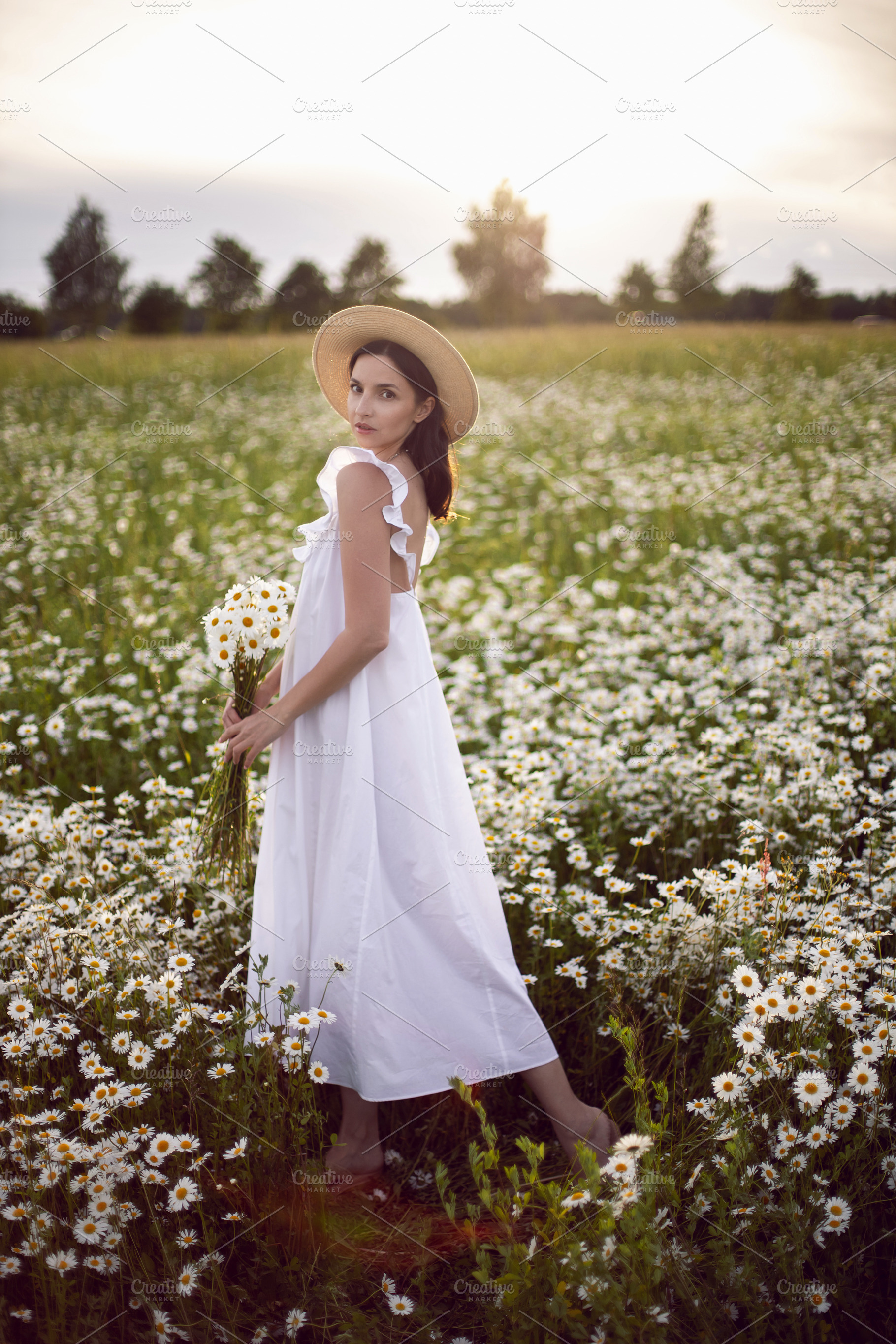 beautiful young brunette woman with long hair in a hat and a white dress is hol, a Person Photo by SaulichPhoto