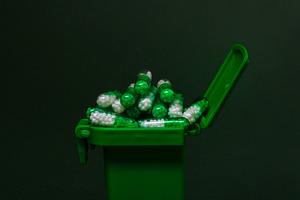 Overflowing green medical waste bin filled with white and green capsules agains, a Health & Medical Photo by Ales Munt