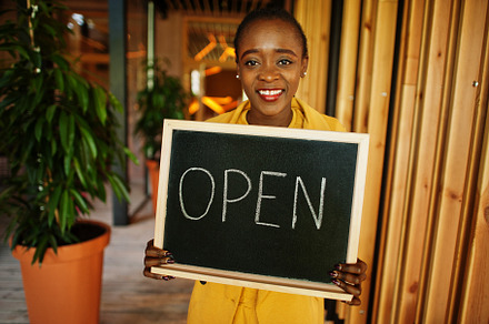 African american woman hold open welcome sign board in modern ca, a Business Photo by AS photostudio