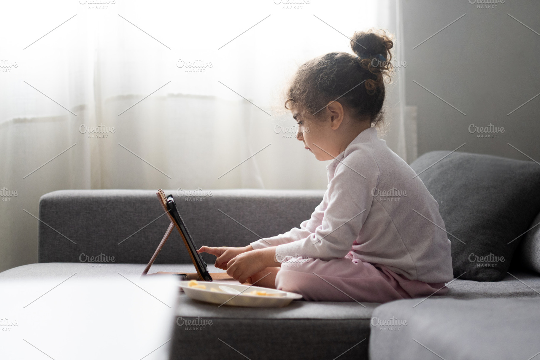 Little girl using tablet on sofa at home, child screen time and digital lifesty, a Food & Drink Photo by etorres69