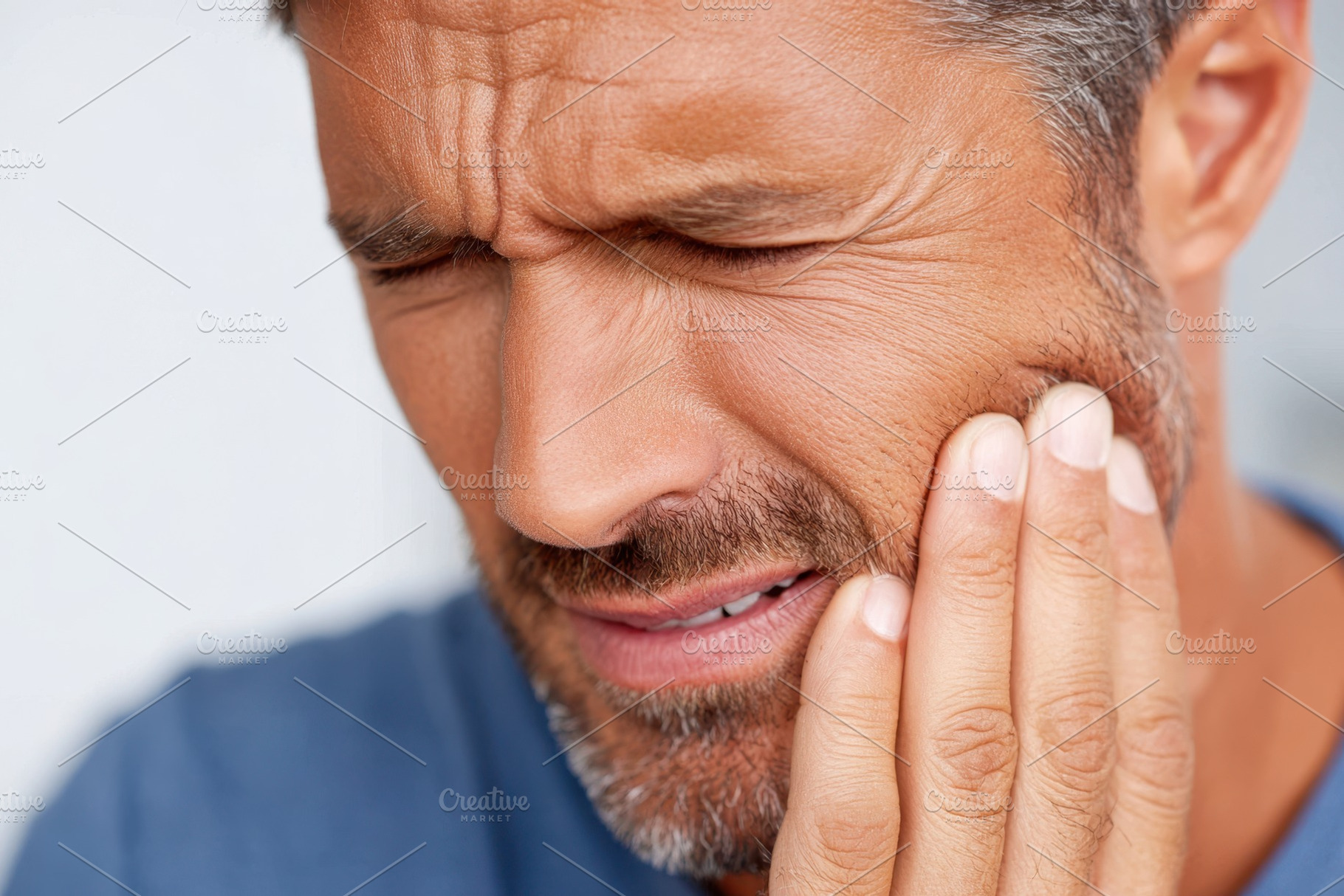 Middle-aged man with hand on cheek in pain because of a toothache, a Health & Medical Photo by AlyaAnd