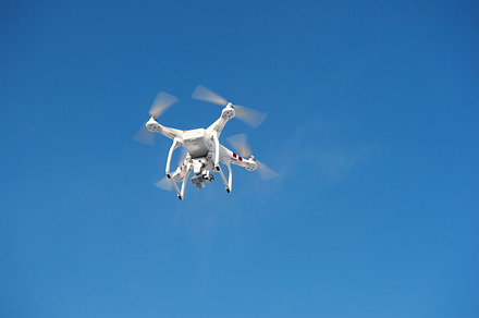 Quadrocopter unmanned camera hovers in bright blue sky containing aircraft