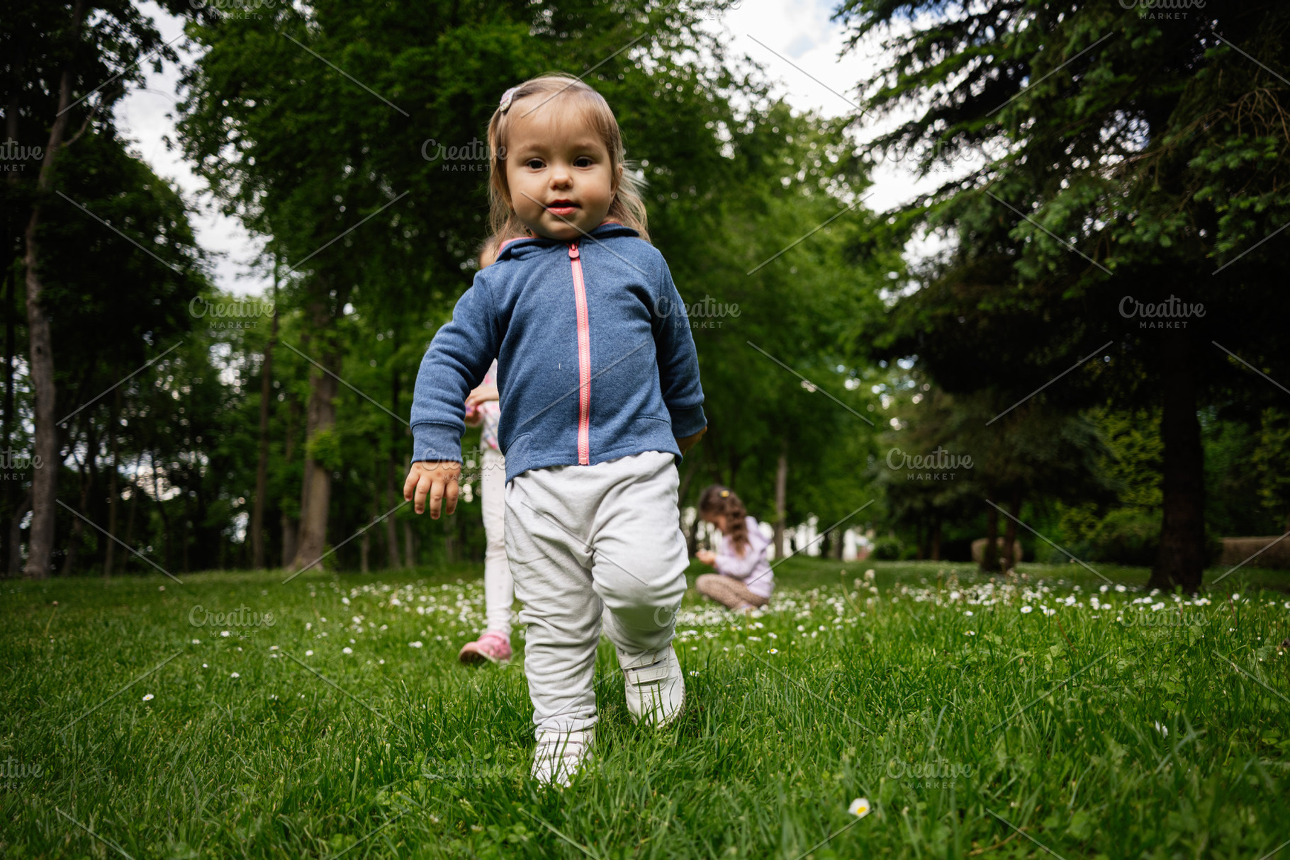 Young child walking in a sunny park with other children playing nearby, a Person Photo by AS photostudio