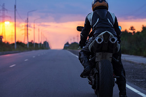 motorcyclist stands on an empty road at sunset , back view , copy space. Travel, a Photo by PavelKant