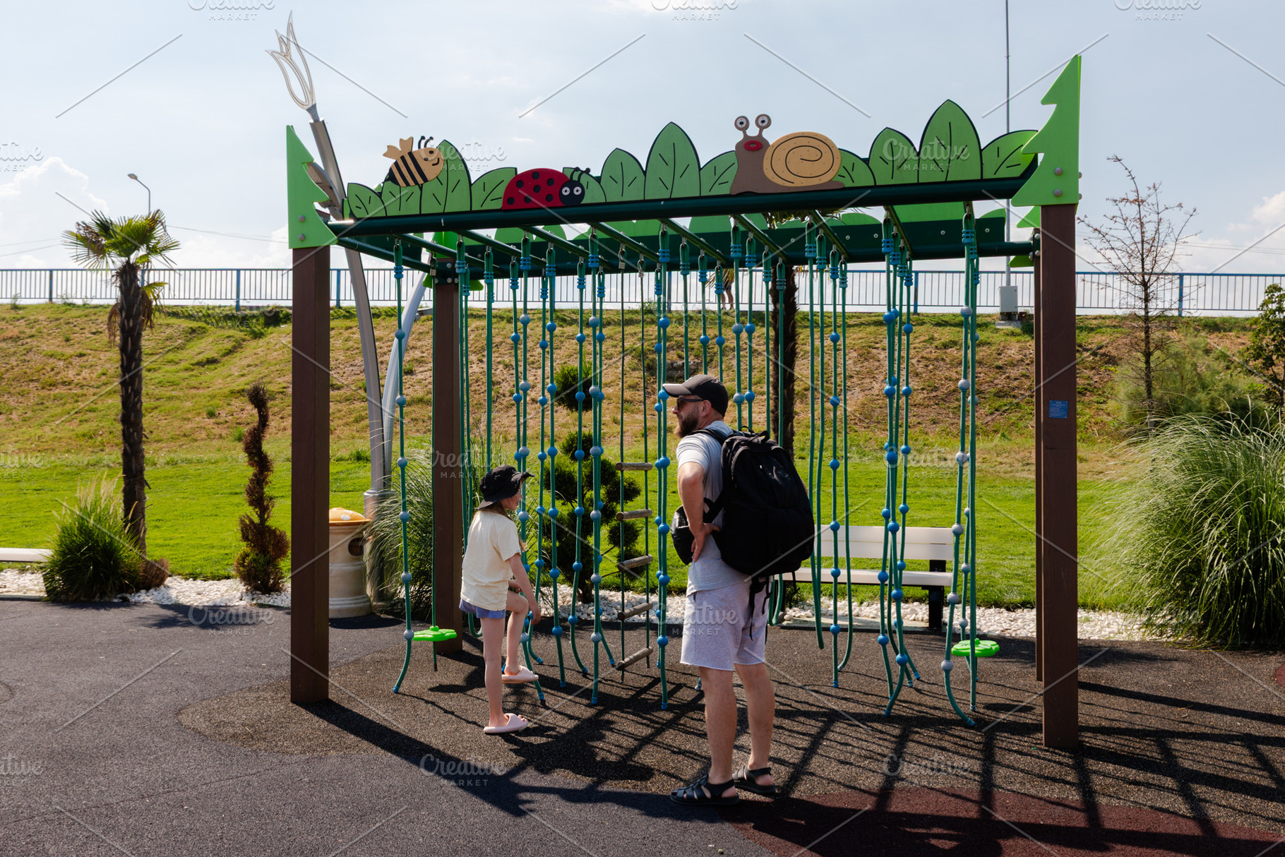Man and young girl standing by a colorful rope climbing frame at an outdoor pla, a Person Photo by Ales Munt