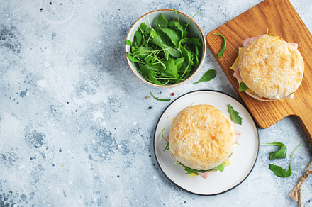 Two homemade sandwiches with ham, cheese and arugula on a concrete table., a Food & Drink Photo by Budarinphoto