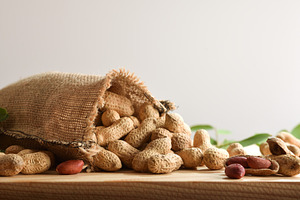 Cloth sack filled with peanuts scattered on table isolated backg, a Food & Drink Photo by Davizro's Market