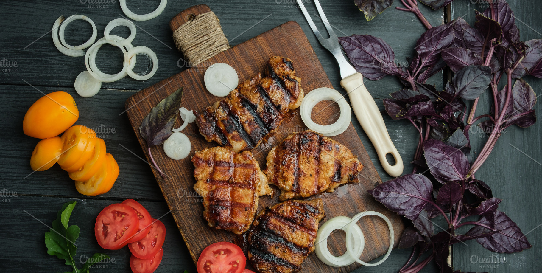 Grilled pork steaks on a wooden board, surrounded by vegetables, a Food & Drink Photo by ndanko