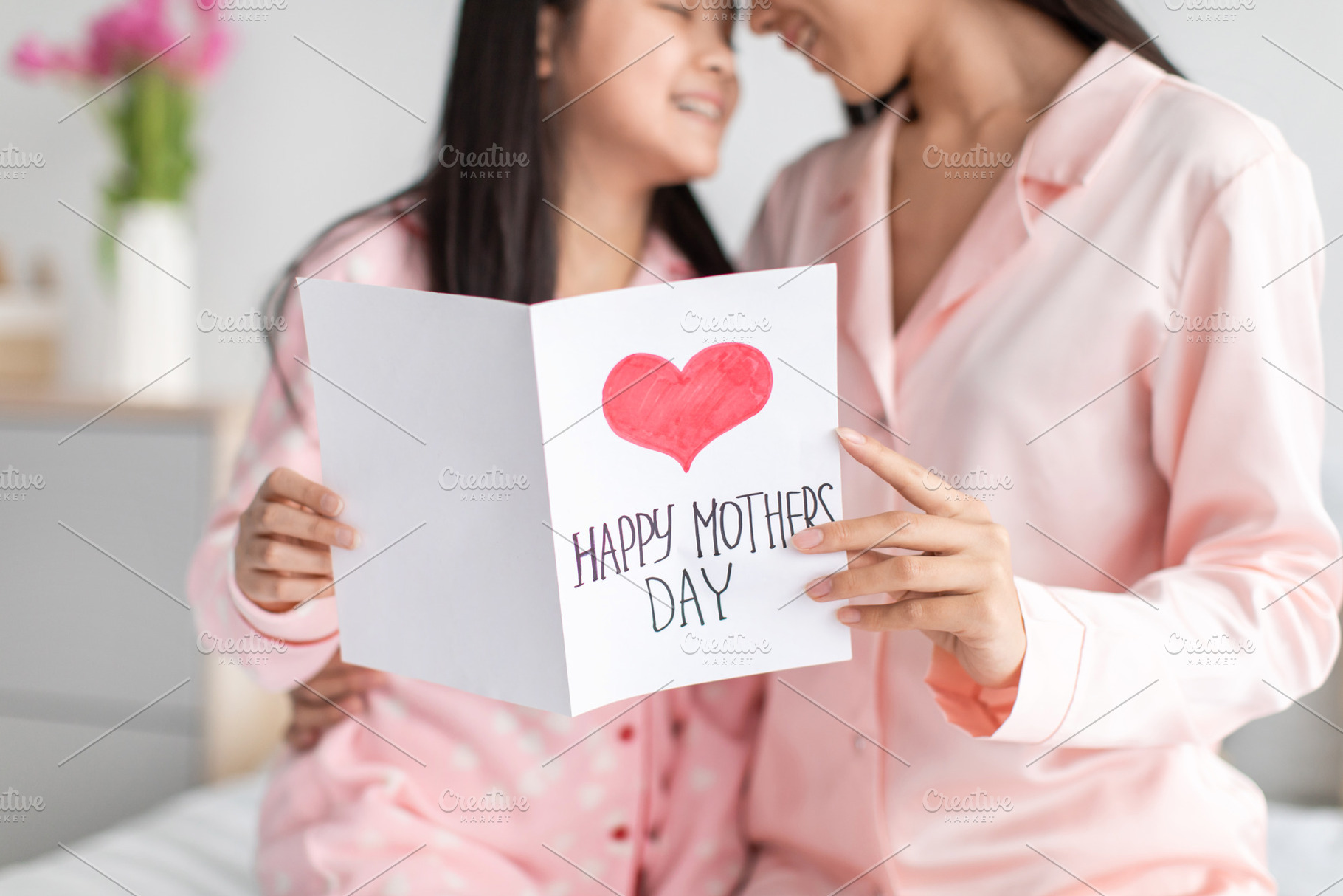 Glad happy teen chinese girl and millennial female in pajamas hold postcard in, a Photo by Prostock-Studio