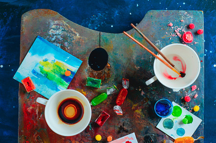 Artist workplace with empty coffee cups, oil and watercolor paint brushes on a colorful palette, sketches and snacks. Flat lay with copy space. Creative occupation concept., a Background Photo by dinabelenko