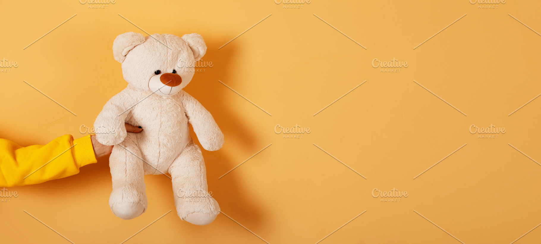 Hand holding a soft plush teddy bear against a vibrant orange ba, a Person Photo by Ales Munt