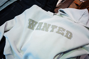 White hoodie with Wanted printed text displayed on a wooden background, a Photo by AS photostudio