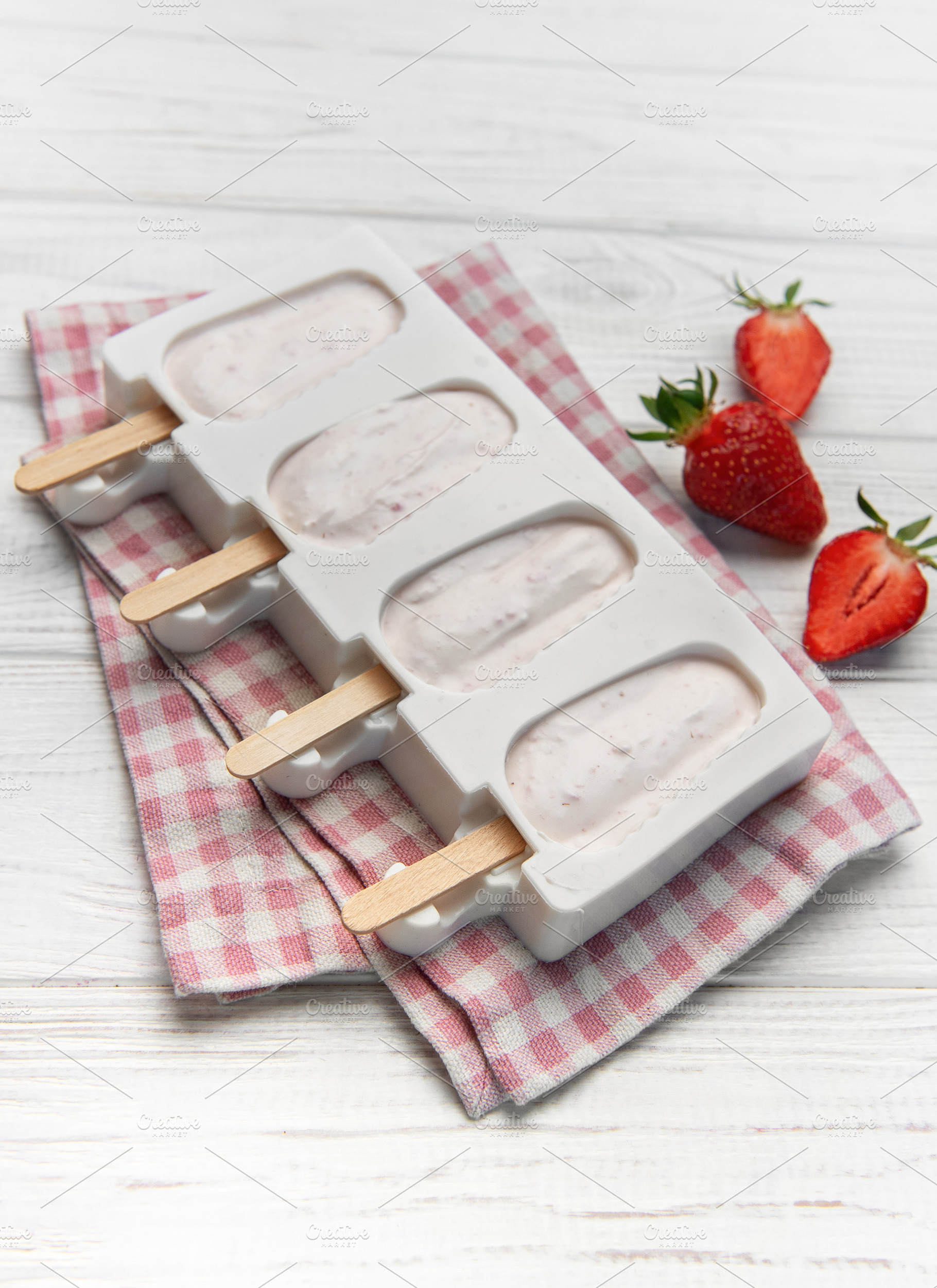 Diy strawberry yogurt popsicles chilling in mold on white wood, a Food & Drink Photo by Olena Rudo