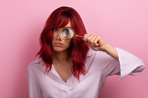 Young woman with red hair examining through a magnifying glass,, a Person Photo by Ales Munt