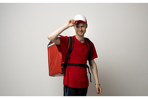 Smiling young delivery man in red, a Person Photo by volodymyrshtun13795