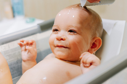 Portrait of a nine month old baby taking a bath with water running trough his f
