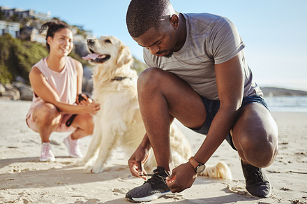 Fitness, walk and couple at the beach with their dog for freedom, exercise and relax during summer. Wellness, nature and black man tying shoelace by the sea before running with his pet and girlfriend, a Photo by Peopleimages.com