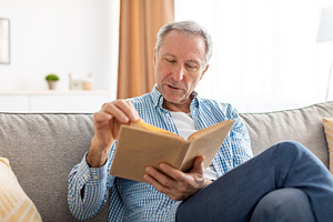 Portrait of mature man reading book at home, a Photo by Prostock-Studio