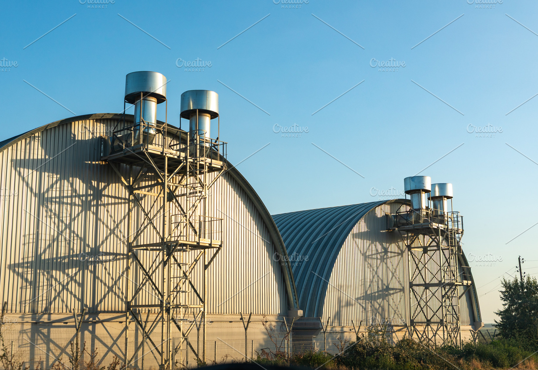 Modern industrial warehouses with metal vents and curved roofs, captured in sof, an Architecture Photo by Ales Munt