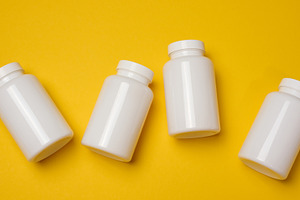 White plastic medicine jars on a yellow background, top view, a Health & Medical Photo by ndanko