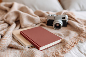 View from above of a blank hardcover resting on a cozy blanket next to a vintag, a Photo by AlyaAnd