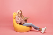 Dreamy lady reading book while sitting in comfortable beanbag chair over pink b, a Photo by Prostock-Studio (Thumbnail 1 of 2)