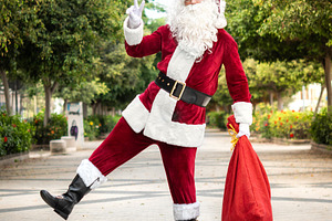 Playful Santa Claus carrying gift sack and making peace sign outdoors, a Person Photo by etorres69