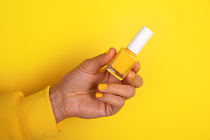 Hand holding yellow nail polish bottle on vibrant yellow backgro, a Beauty & Fashion Photo by Ales Munt