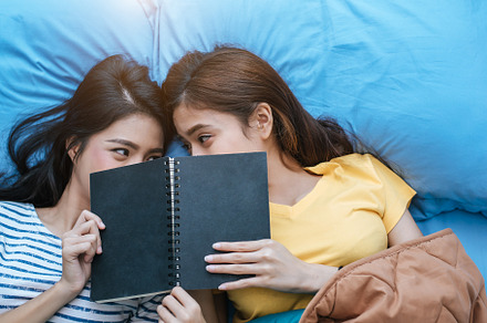 Cute Asian lesbian couple reading book together and lying on bed, a Person Photo by Ministocker
